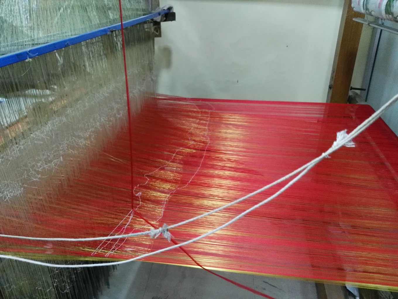 Red silk and gold zari threads stretched across the loom
